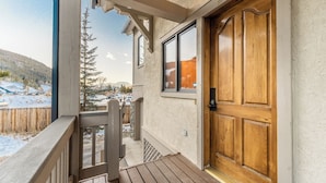 A wooden door with a number plate, a balcony with a wooden railing, and a view of a snowy landscape with trees and mountains in the background. - Iw2997-3 (Keystone)