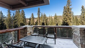 A balcony with a table and chairs, a stone wall, and a view of tall trees. - T30734 (Keystone)