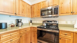 A kitchen with wooden cabinets, a stainless steel microwave, a stove, and a coffee maker. - Expedition Station #8581 (Keystone)