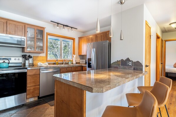 Una cocina moderna con armarios de madera, electrodomésticos de acero inoxidable, encimera de granito y una ventana con vistas a la montaña.