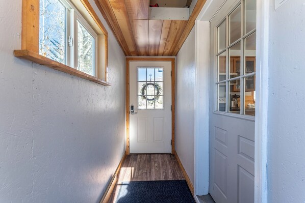 Un pasillo estrecho con vigas de madera, una puerta blanca con un adorno y una ventana a la izquierda.