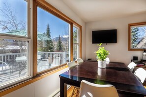 A dining area with a large table, chairs, a potted plant, and a TV mounted on the wall.