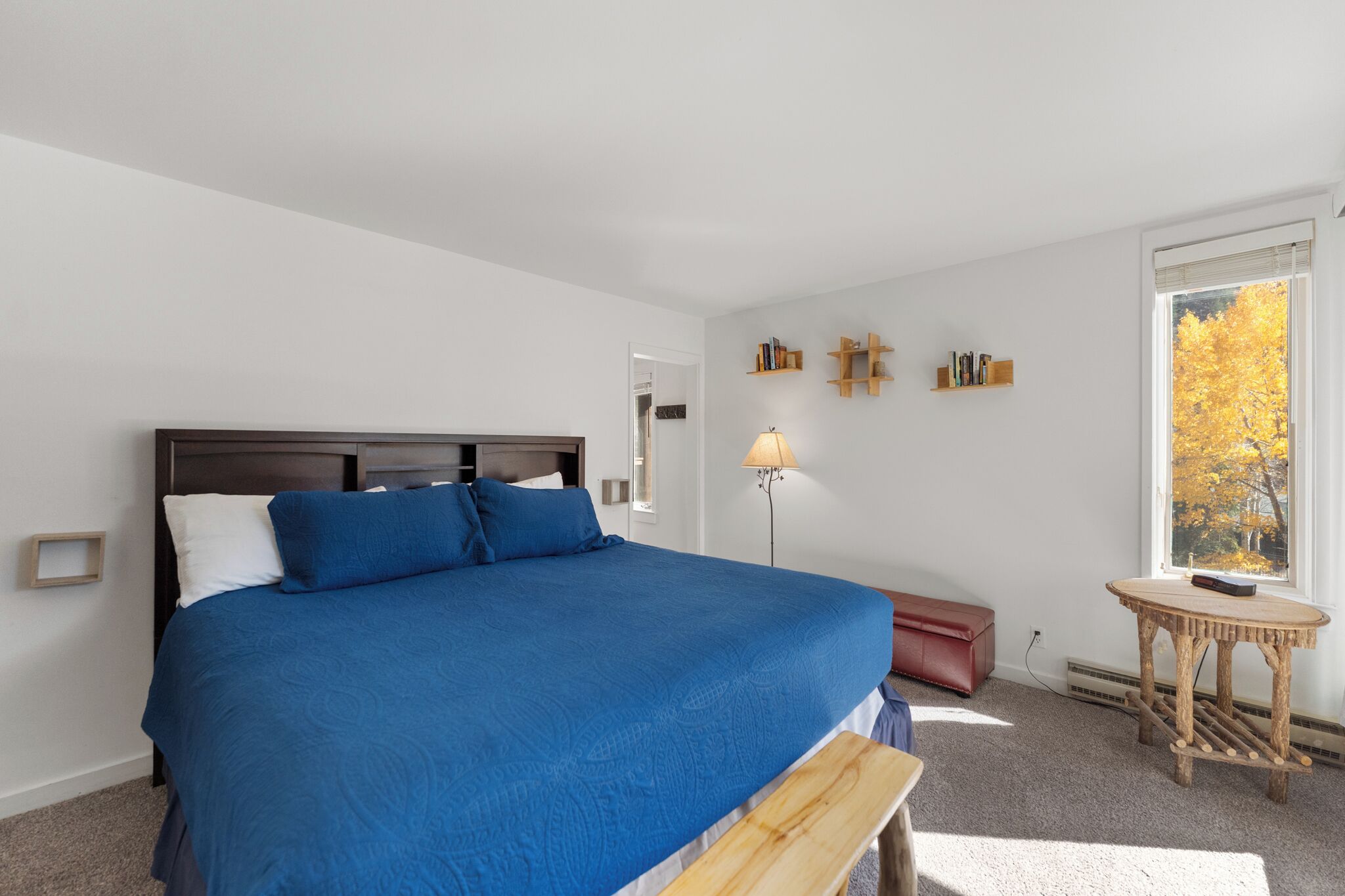 A bedroom with a large bed, a bedside table, a lamp, and a window with a view of trees.