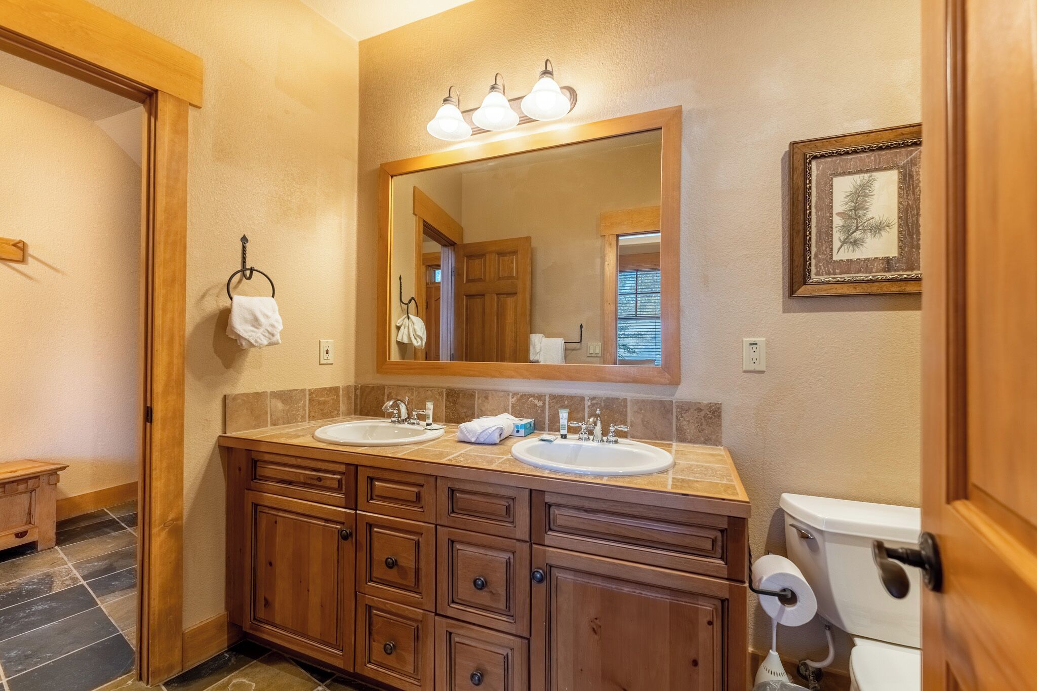 A bathroom with two sinks, wooden vanity, a large mirror, and a framed picture on the wall.