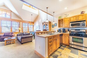 A spacious living area with a kitchen, wooden cabinets, and a large island with a sink.