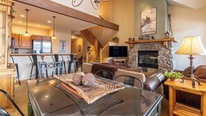 A spacious living area with a dining table, leather sofas, a stone fireplace, and a kitchen in the background. - Er9576k2 (Keystone)