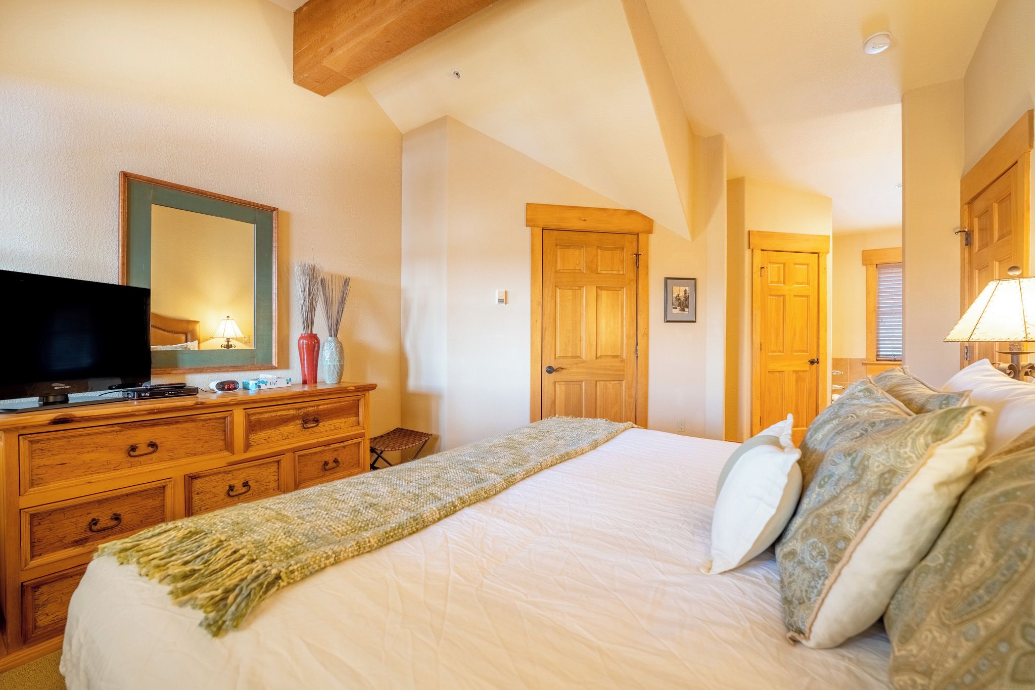 A bedroom with a large bed, wooden dresser, television, and a mirror.