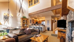 A spacious living room with a large sofa, a coffee table, and a fireplace. There is a kitchen area with wooden cabinets and a dining table. - Er9576k2 (Keystone)