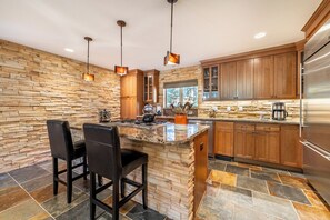 A modern kitchen with a stone backsplash, wooden cabinets, and a large island with bar stools.