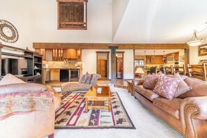 A spacious living area with a fireplace, leather sofas, a coffee table, and a kitchen in the background.