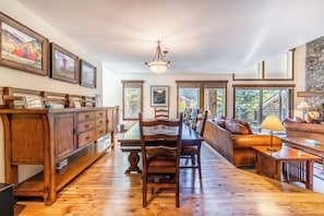 A spacious living area with a wooden dining table, chairs, a sofa, and a coffee table. There are framed pictures on the walls and a stone accent wall.