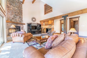 A spacious living room with a stone wall, leather sofas, a fireplace, and a kitchen area.
