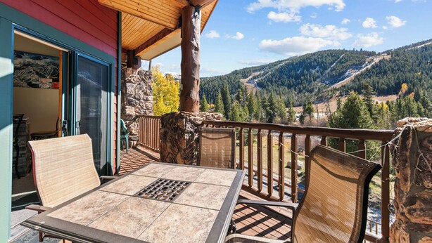 Une terrasse en bois avec une table et des chaises, offrant une vue sur un paysage montagneux.