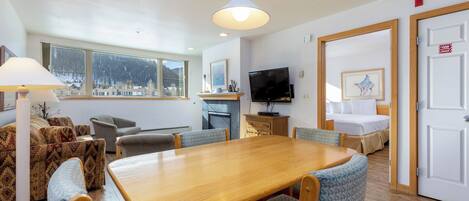Una habitación con una mesa de comedor de madera, sillas con estampado azul, un sofá, un televisor y una cama.