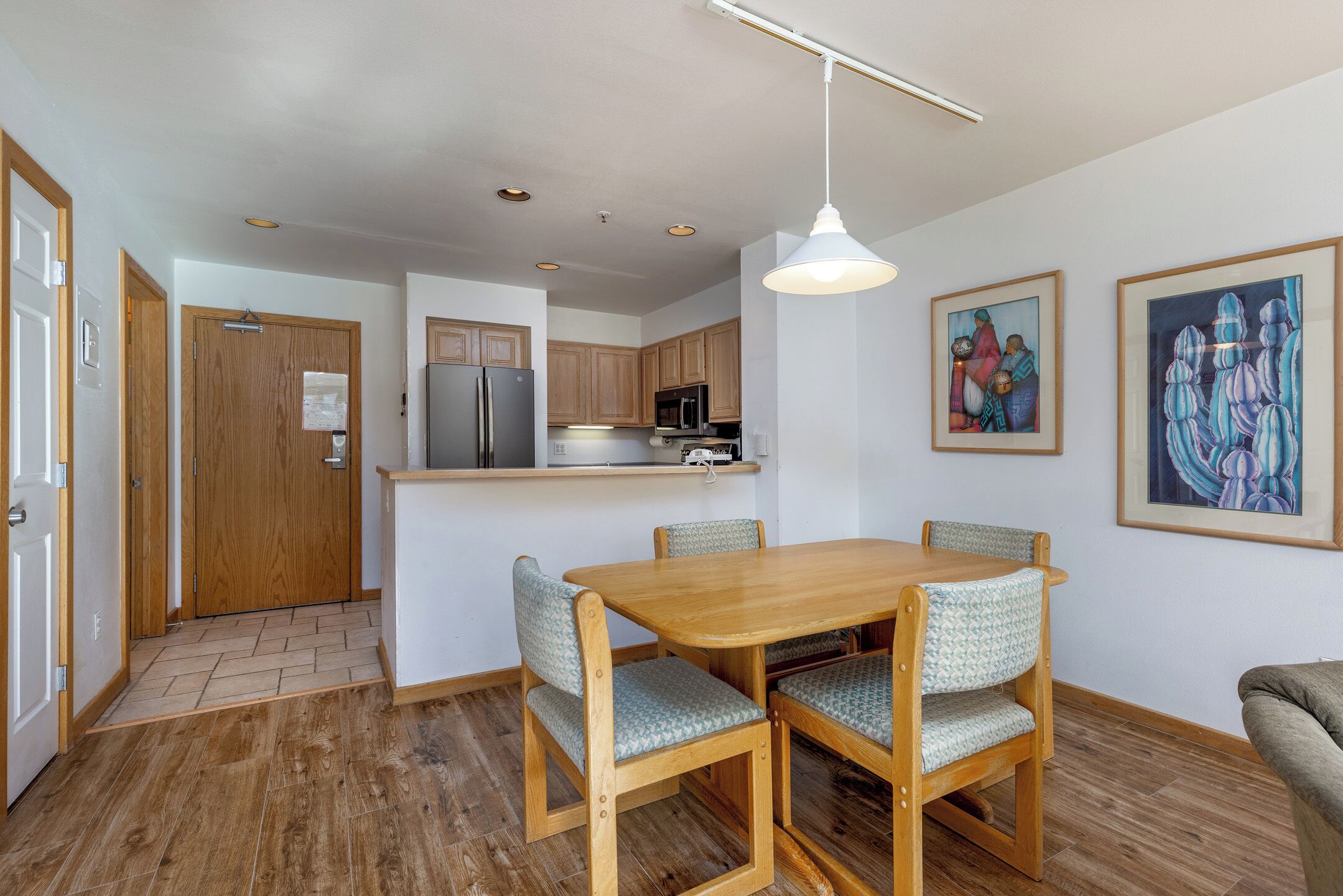 A modern kitchen with wooden cabinets, a built-in refrigerator, and a dining area with a wooden table and patterned chairs.