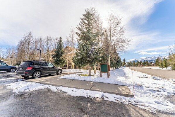 A parking lot with a black SUV parked near a green mailbox and a tree.