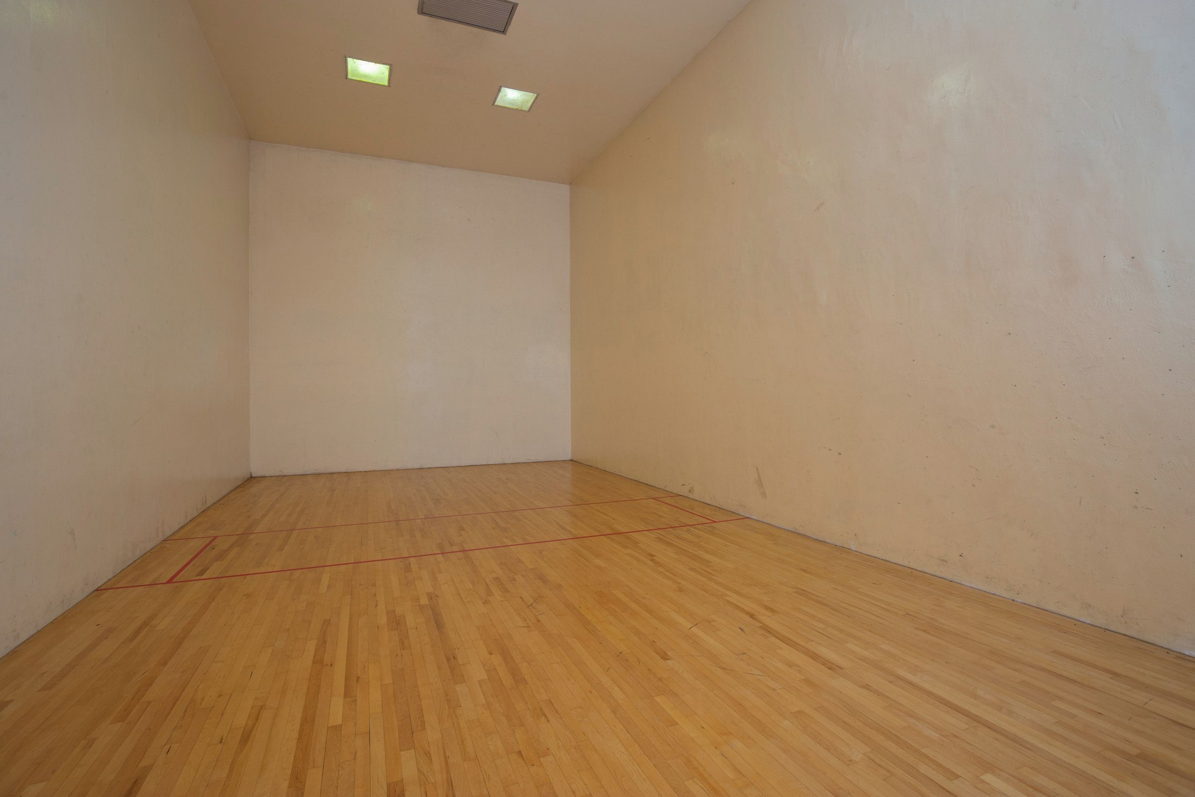 A squash court with wooden flooring and white walls.