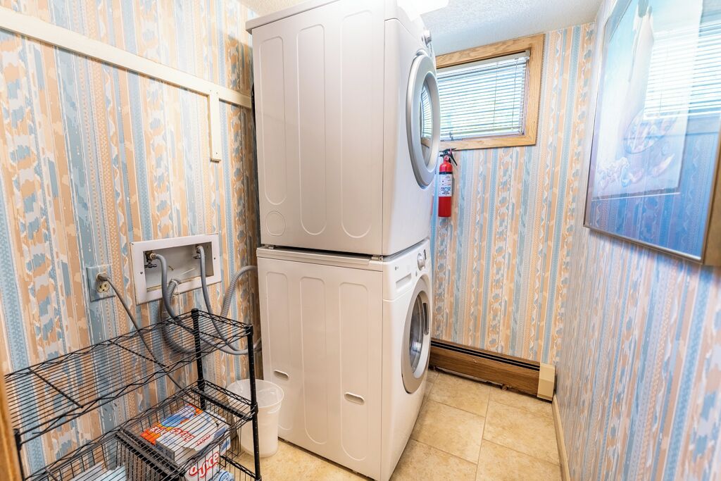 A compact laundry room with a stacked washer and dryer, a metal drying rack, and a fire extinguisher mounted on the wall.