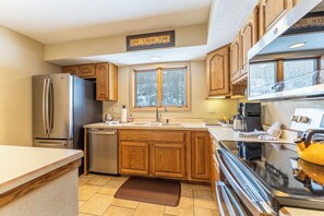 A kitchen with wooden cabinets, a stainless steel refrigerator, a dishwasher, a sink, and a stove.