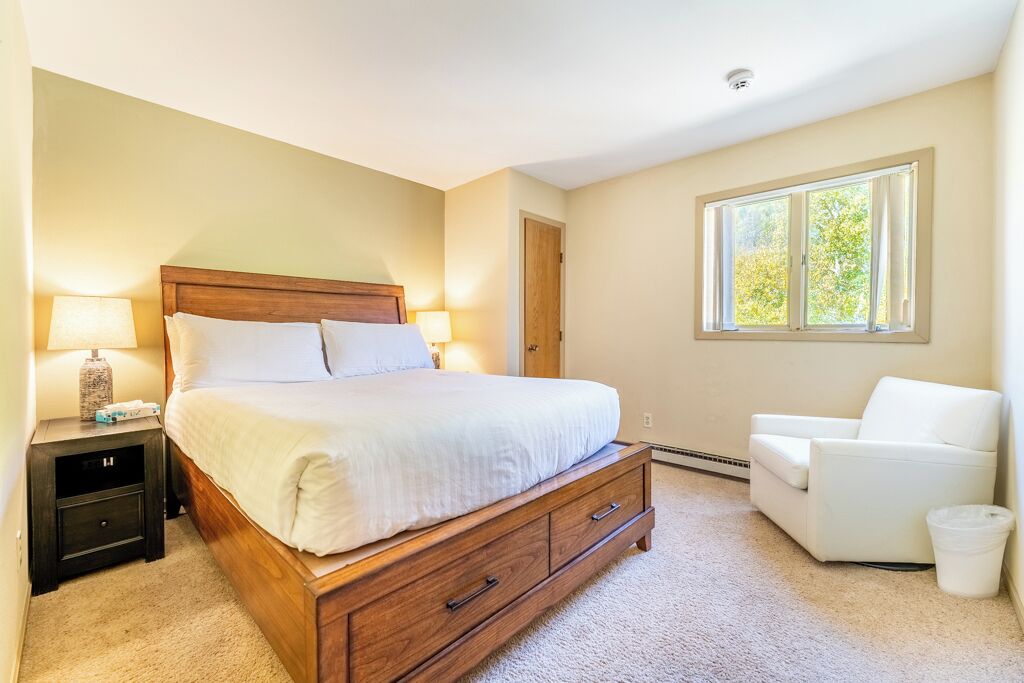A bedroom with a wooden bed, bedside tables, a chair, and a window.