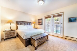 Un dormitorio con una cama grande, dos mesitas de noche, un banco de madera y un ventanal corredero que da a un balcón.