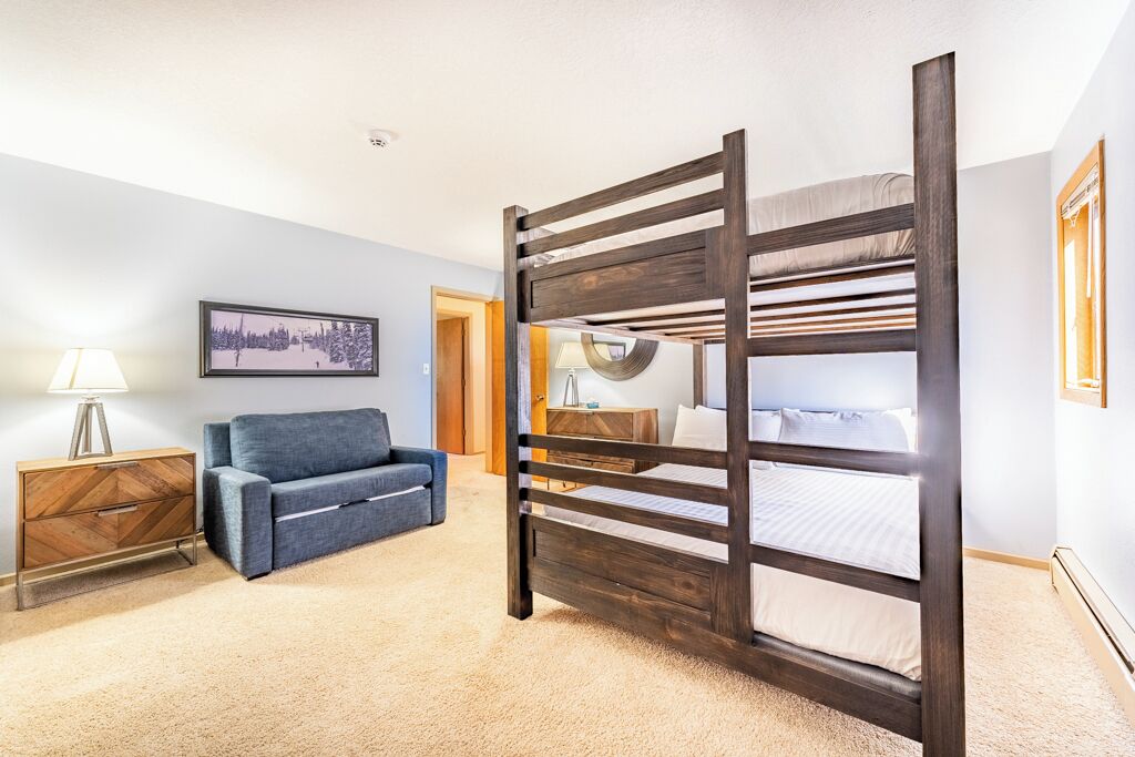A room with a bunk bed, a sofa, a lamp, and a framed picture on the wall.