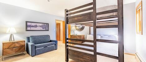 A room with a bunk bed, a sofa, a lamp, and a framed picture on the wall.