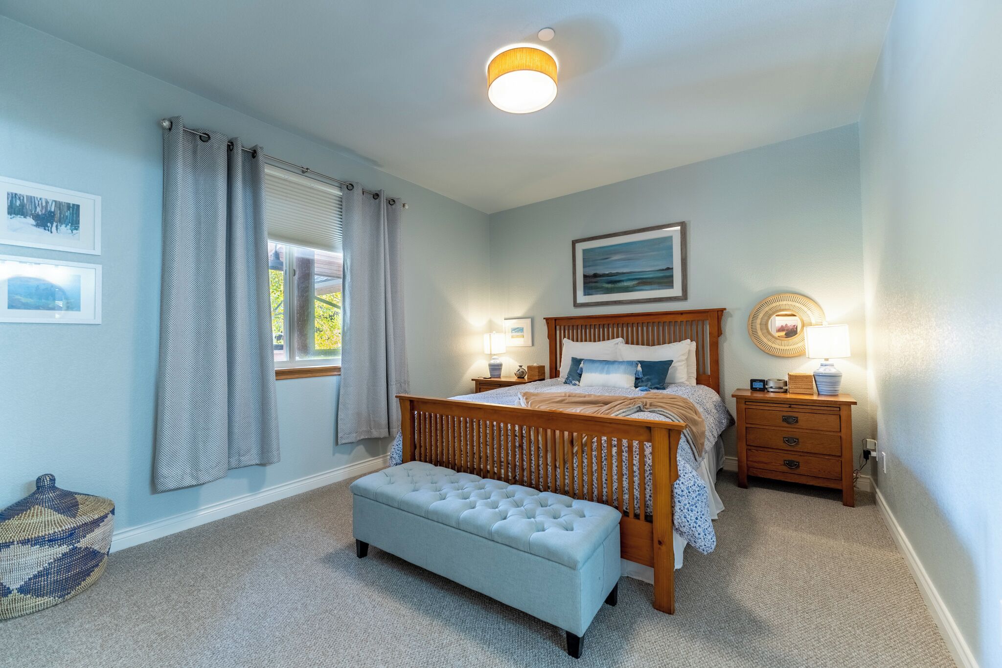 Un dormitorio con cama, mesitas de noche, un banco y una ventana con cortinas.