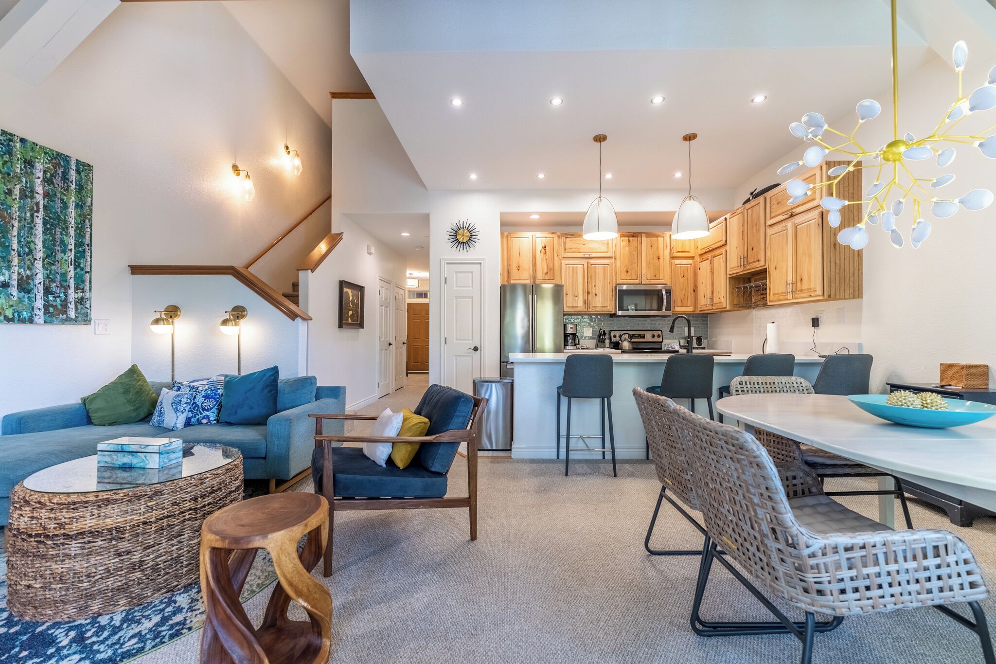 A modern kitchen with wooden cabinets, a stainless steel refrigerator, and a dining area with a white table and wicker chairs.