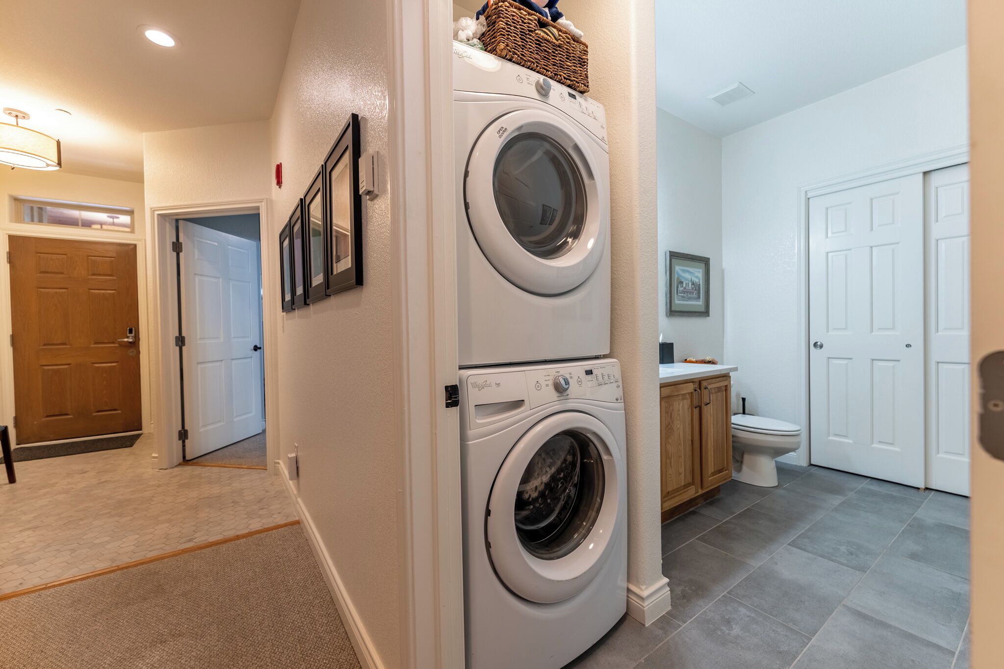 A laundry room with two stacked front-loading washing machines, a wooden cabinet, and a toilet.