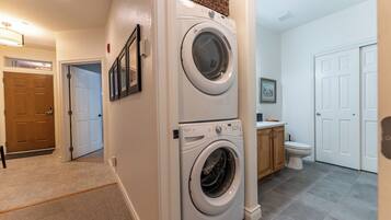 A laundry room with two stacked front-loading washing machines, a wooden cabinet, and a toilet.