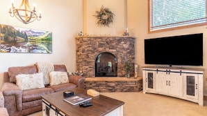 A living room with a stone fireplace, a large flat-screen TV, a brown leather sofa, and a wooden coffee table. - Ab22-3 (Keystone)