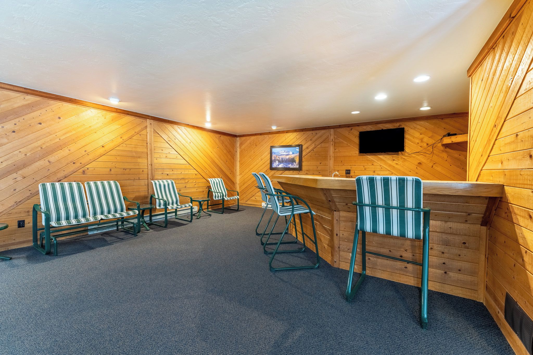 Quarto com paredes de madeira, área de bar e várias cadeiras listradas.
