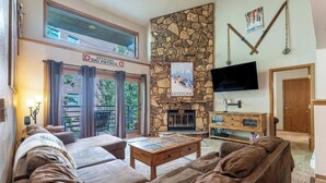 Un salon chaleureux avec une cheminée en pierre, un téléviseur à écran plat et un panneau indiquant le service de patrouille de ski de Keystone.