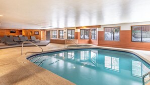 Une piscine intérieure offrant une vue dégagée sur les environs, avec notamment un espace détente comprenant des chaises et un mur en bois.