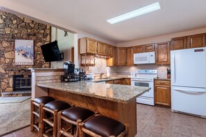 A kitchen with wooden cabinets, a granite countertop, a stone fireplace, and a bar area with stools.