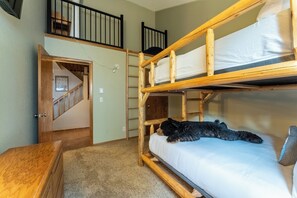 A bunk bed room with a wooden ladder, a small desk, and a staircase leading to an upper level.