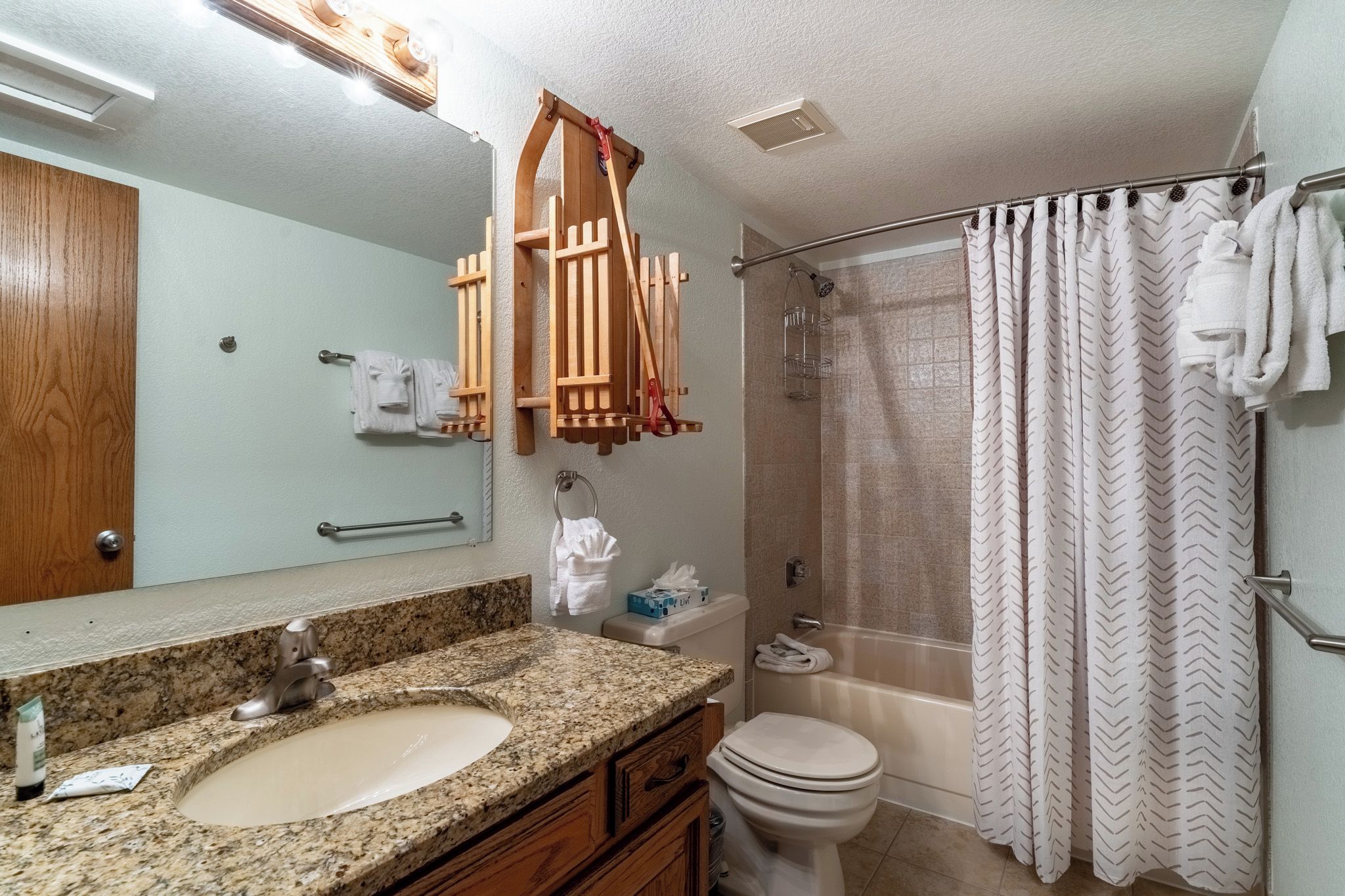 A bathroom with a granite sink, wooden vanity, a toilet, a shower with a glass door, and a mirror with a wooden frame.