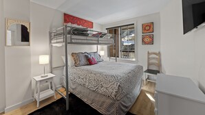 A bunk bed room with a patterned bedspread, a small bedside table with a lamp, a chair, and a TV on the wall. - Dakota Lodge #8492 (Keystone)