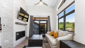 A modern living room with a stone fireplace, a flat-screen TV, a sofa with cushions, and large windows offering a mountain view. - Skywalk Flats #305e : 2 (Silverthorne)
