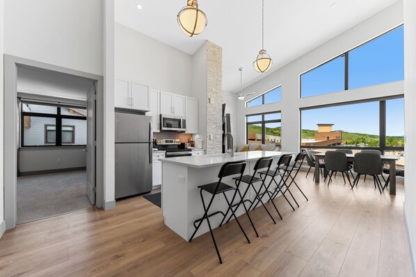 A modern kitchen with a central island, white cabinetry, and large windows offering a view of the outdoors.
