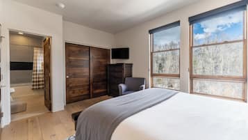 Un dormitorio con una cama grande, un armario de madera, un televisor y una ventana con vistas al bosque.