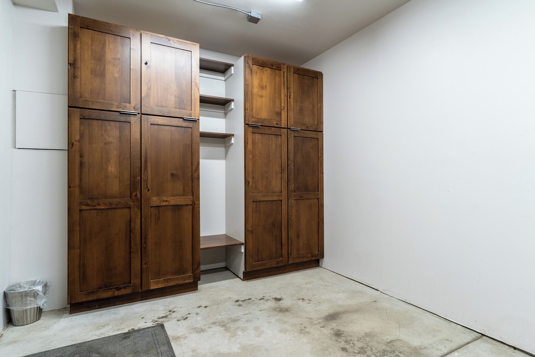 A room with a wooden wardrobe, a small bench, and a trash bin.