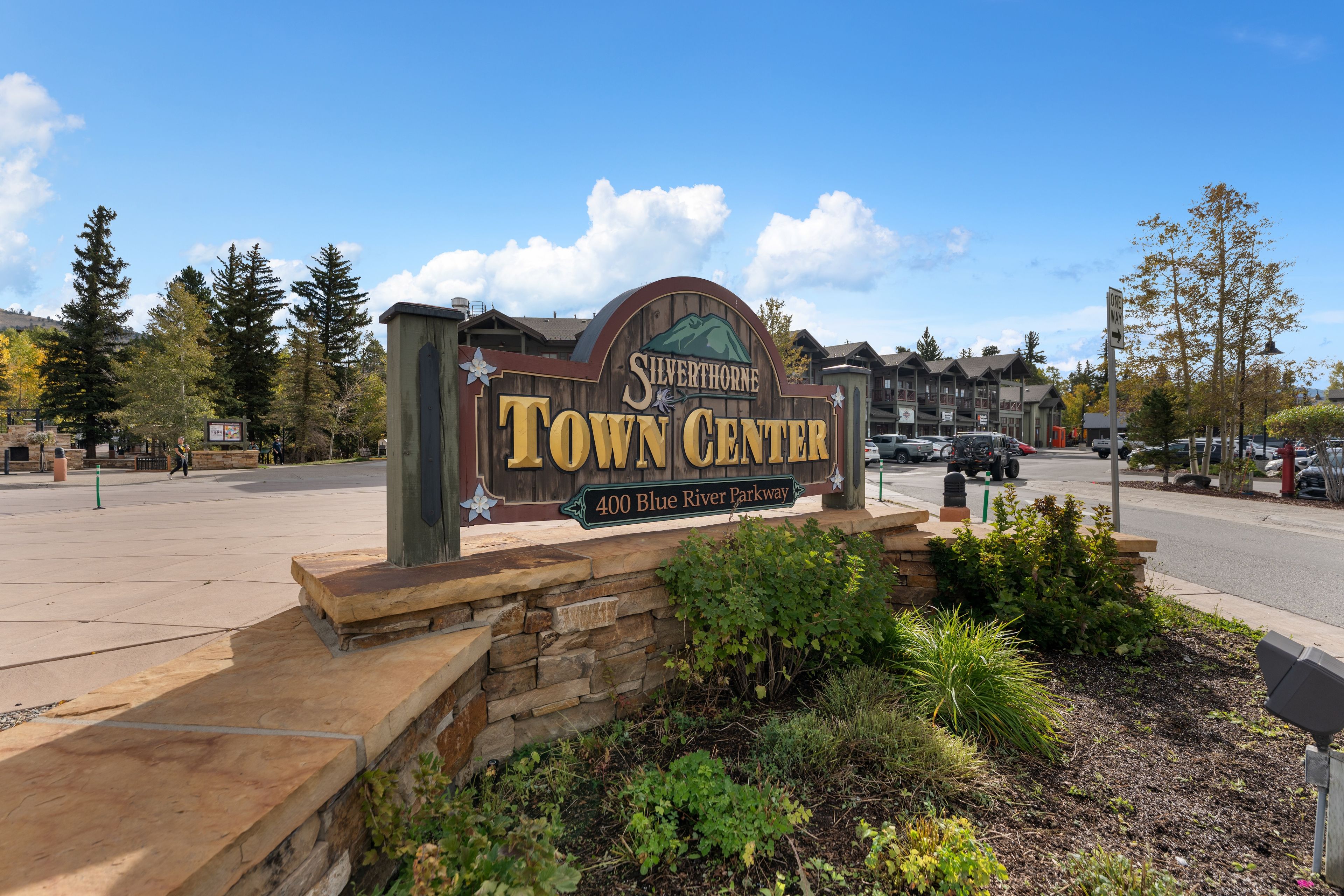 Un panneau en bois indiquant l’entrée du centre-ville de Silverthorne, avec un socle en pierre et des espaces verts aménagés autour.