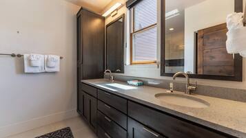 A modern bathroom with two sinks, dark cabinetry, a large mirror, and a window.