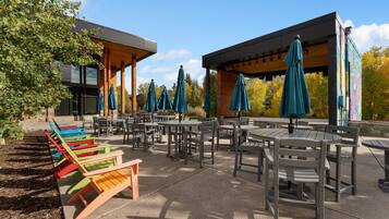 An outdoor seating area with tables and chairs, surrounded by trees and a building with a modern design.