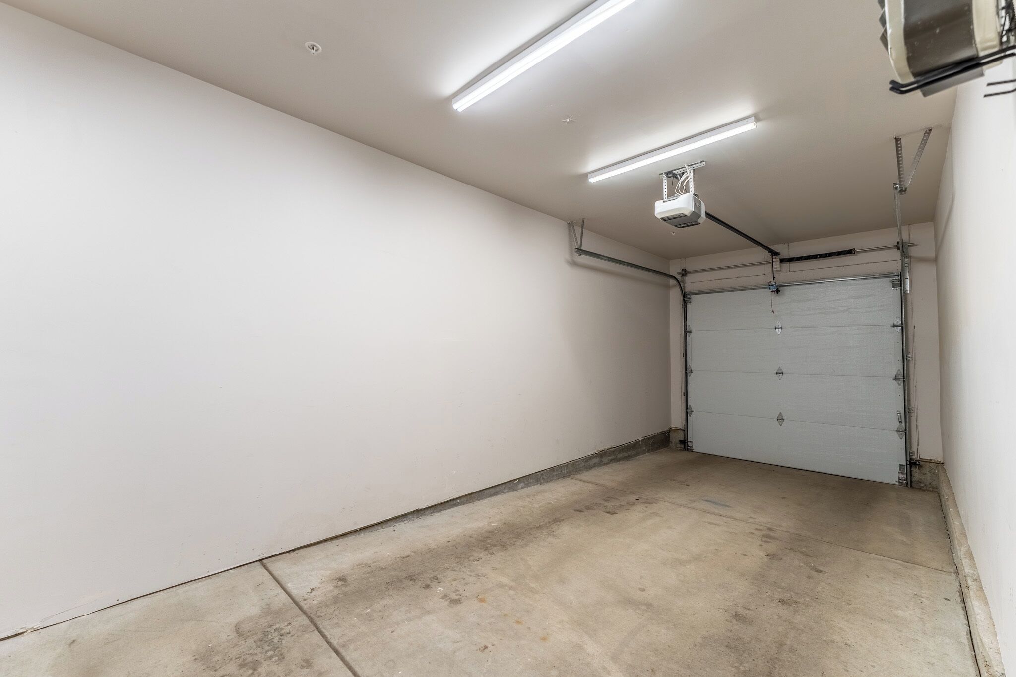A clean, empty garage with white walls, a closed garage door, and fluorescent lighting.