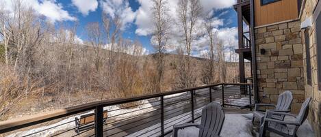 A balcony with Adirondack chairs, a stone wall, and a view of a snowy landscape with trees.