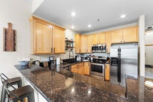 Una cocina moderna con encimeras de granito, electrodomésticos de acero inoxidable, armarios de madera y taburetes de bar.