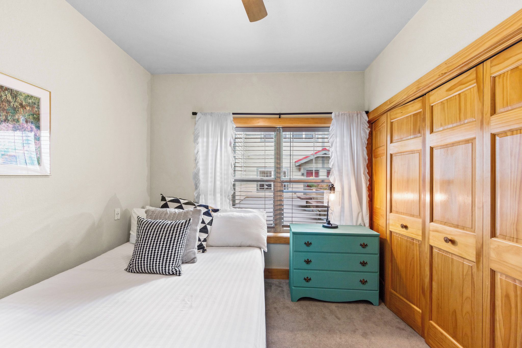 A bedroom with a bed, a window with curtains, a green nightstand, and wooden wardrobe.